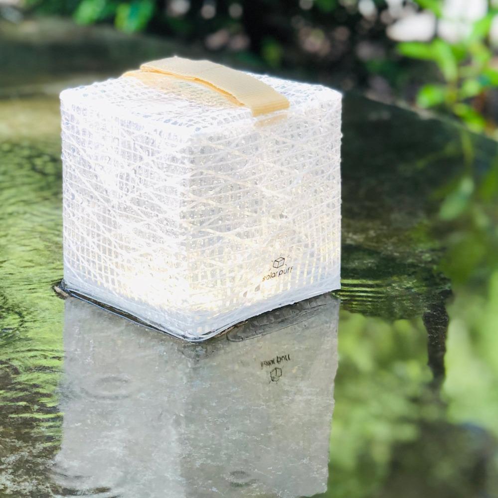 Waterproof SolarPuff lantern on wet sidewalk in outdoor nature scene