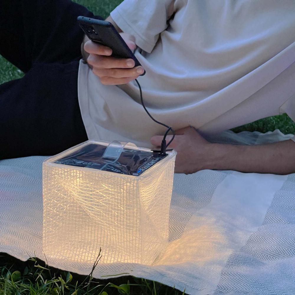 Man charging phone with MEGAPUFF solar lantern on blanket in park