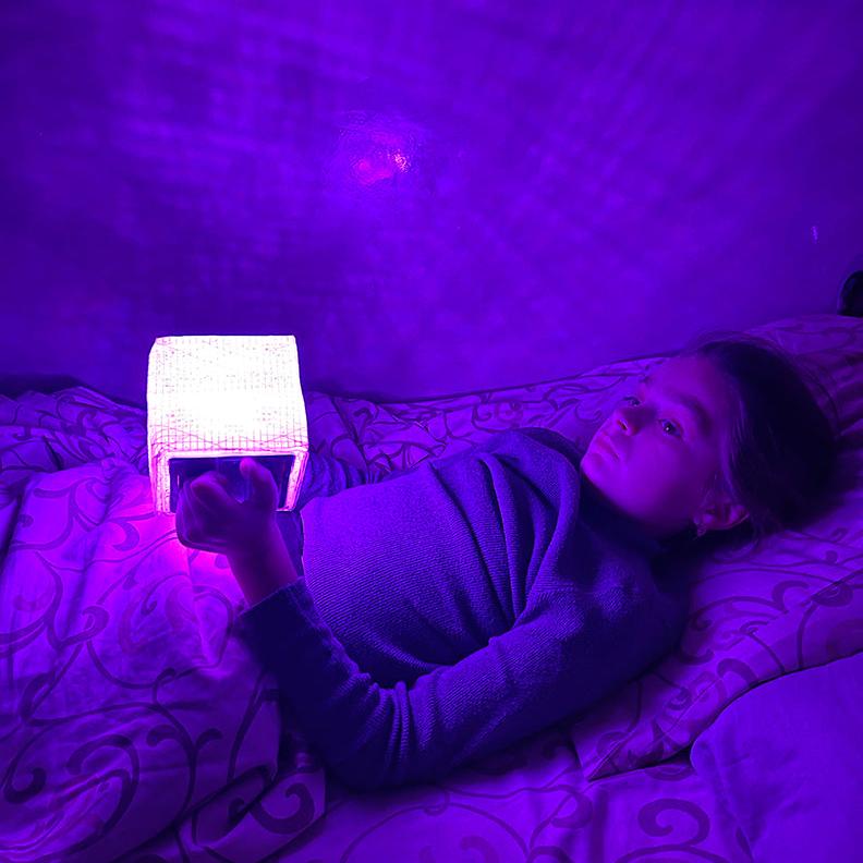 Child laying in bed holding purple lantern.