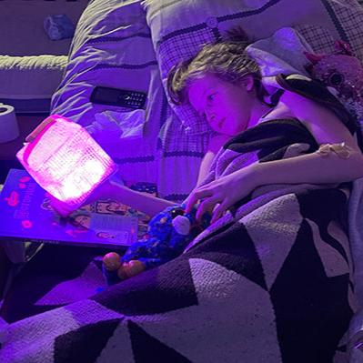 Young Ukrainian girl holding purple lantern in bed.