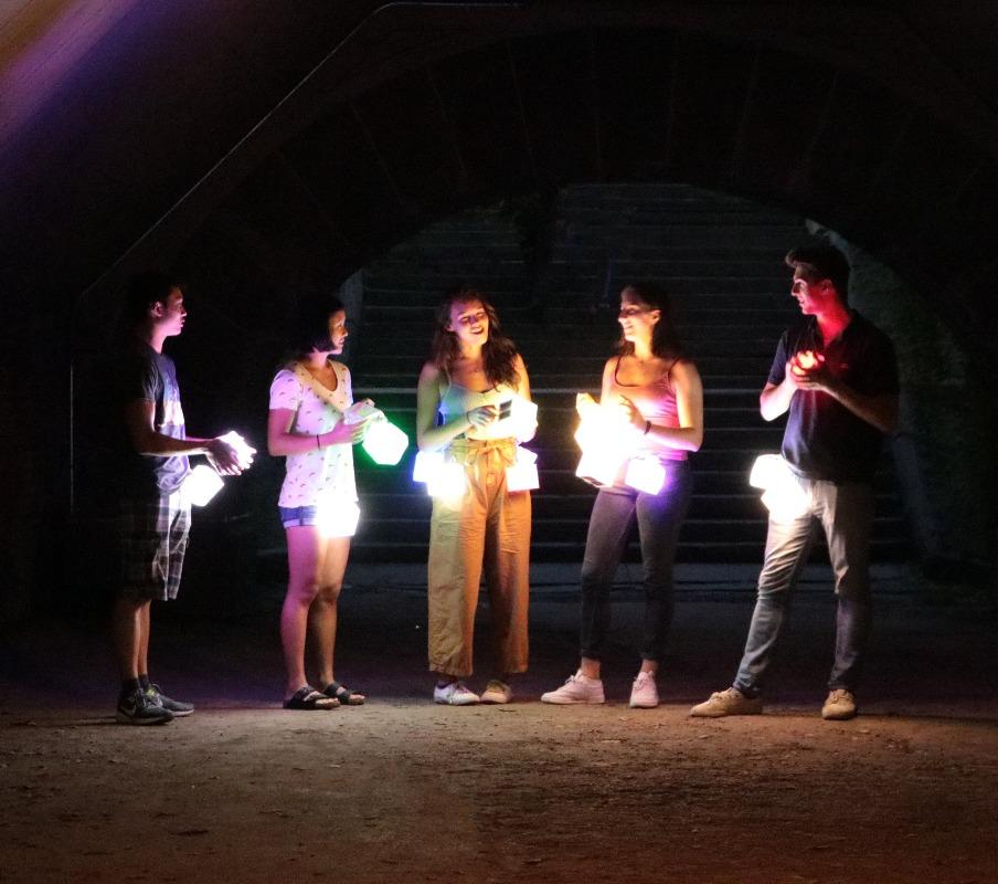 Solar-Lanterns-color- shows a group of teenagers with our multi-color lights in a central park party -they are holding our solar lamps settings on blue, green, and pink- our lamps are perfect for any party -indoor -outdoor-solar-lamp